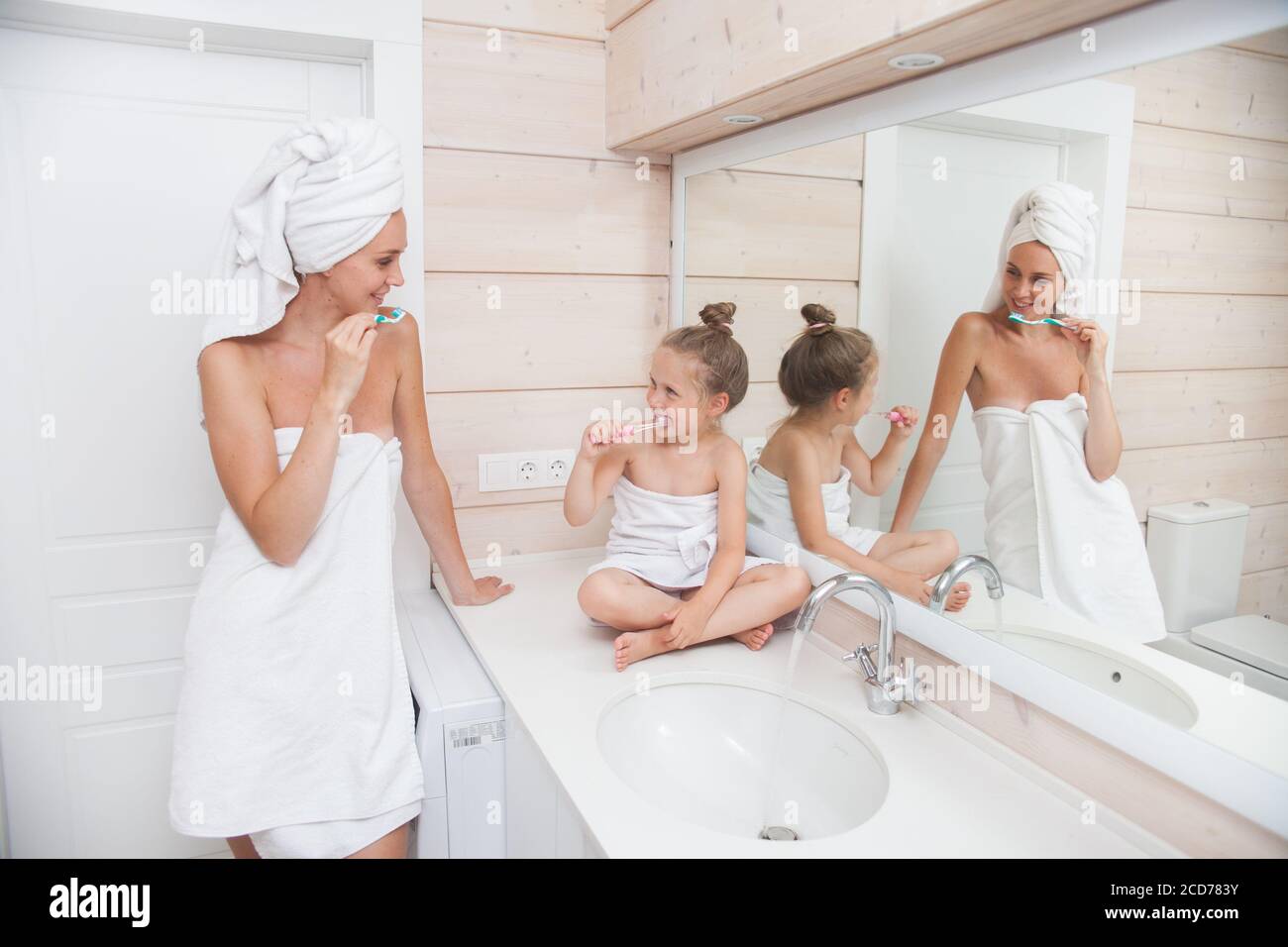 Felice famiglia amorevole spazzolando i denti e passare il tempo insieme. Madre e sua figlia bambina si baciano e abbracciano in bagno bianco. Donna e. Foto Stock