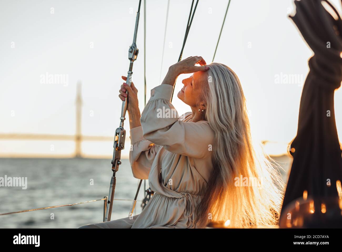 Vista laterale di una donna matura seduta su uno yacht e regolare i capelli al tramonto Foto Stock