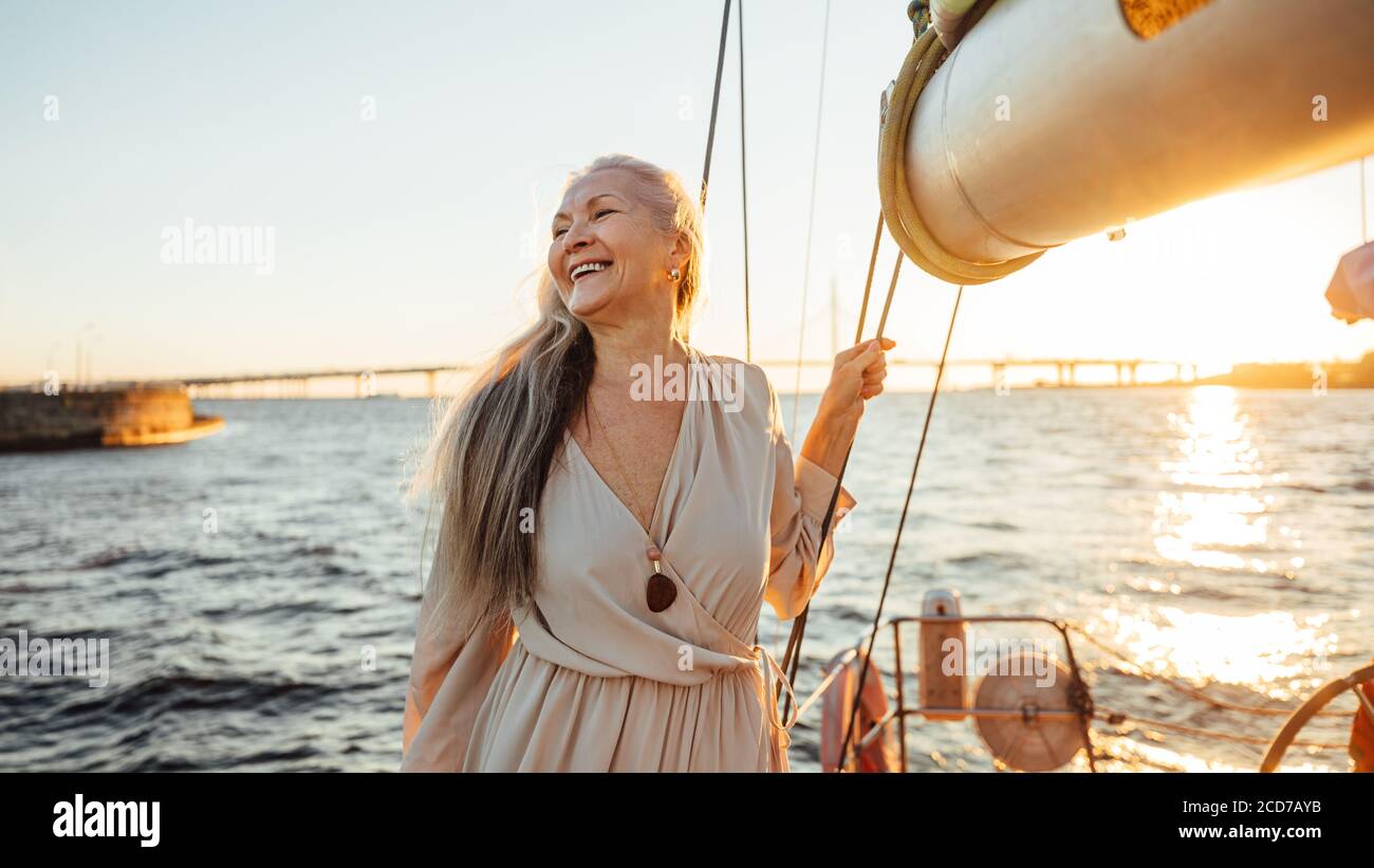 Felice donna matura in piedi su uno yacht al tramonto e. guardando via Foto Stock