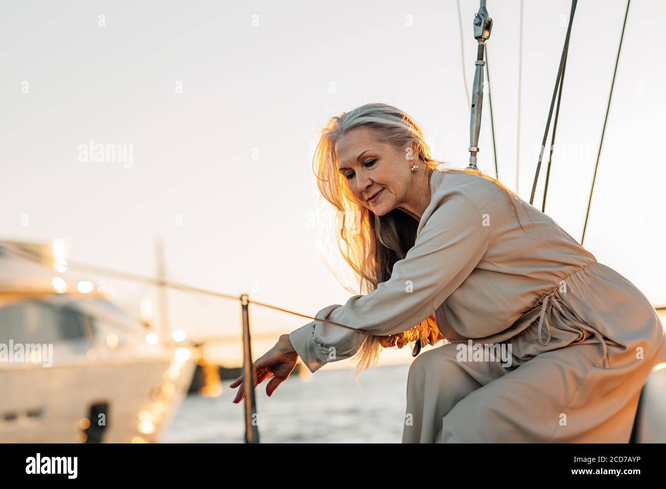 Donna matura ed elegante seduta su un ponte di yacht e guardando su acqua Foto Stock