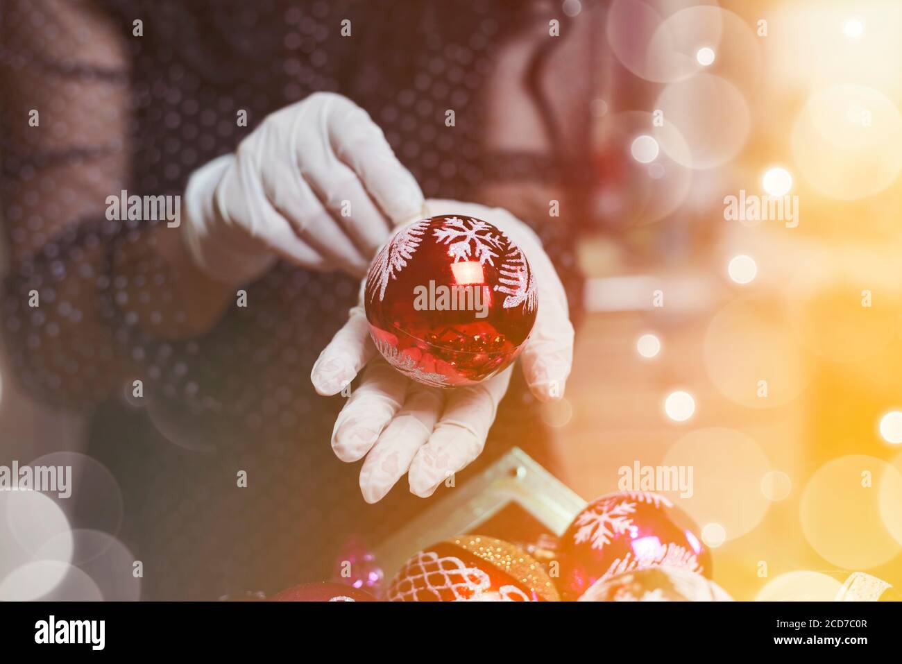 Femmina che tiene il giocattolo di natale. Una donna in guanti medici che prepara decorazioni natalizie. Covid-19 e concetto di Natale Foto Stock