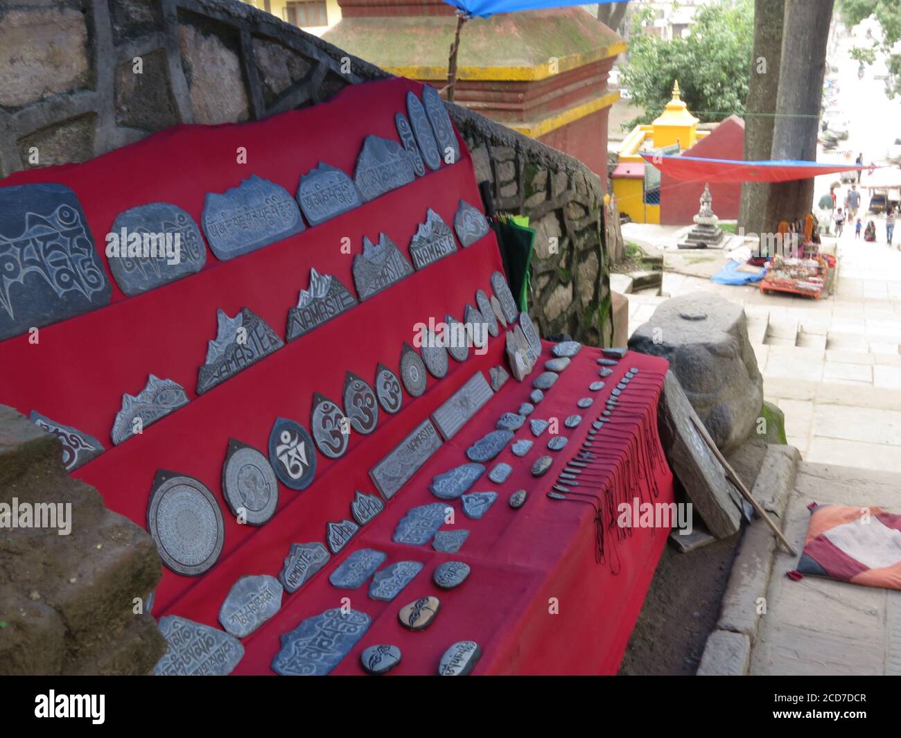 Una pietra di preghiera scolpita con mantra tibetani mostra nel mantello rosso per la vendita nella strada di Kathmandu, Nepal. Foto Stock