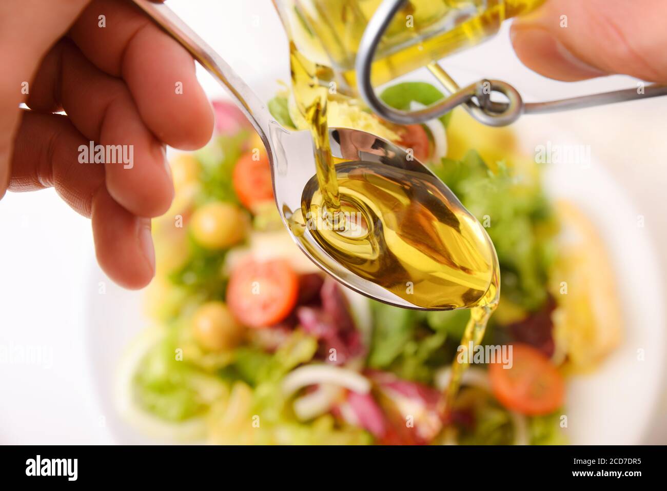 Persona che versa l'olio da una bottiglia di olio di vetro su un cucchiaio per  condire l'insalata. Vista dall'alto Foto stock - Alamy