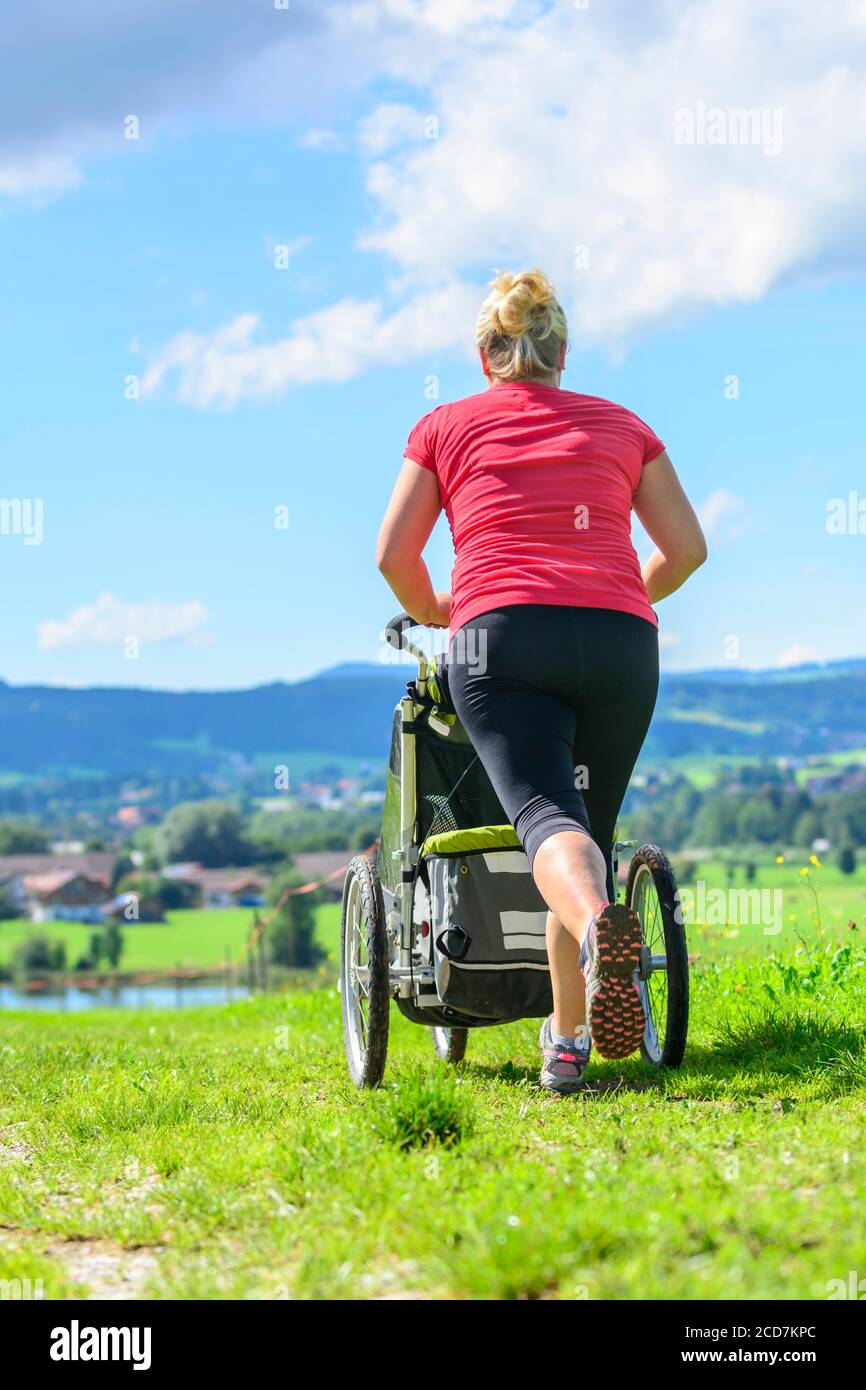 Donna che fa una sessione di jogging con il figlio in buggy dentro bellissimo paesaggio Foto Stock