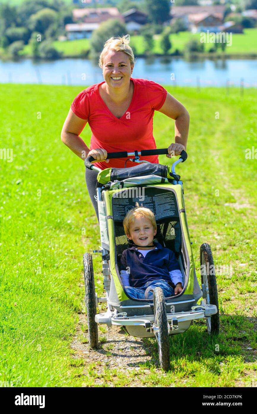 Donna che fa una sessione di jogging con il figlio in buggy dentro bellissimo paesaggio Foto Stock