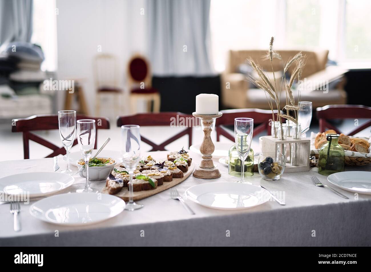 tavolo in stile rustico, spuntini leggeri, candele, piatti su tovaglia bianca Foto Stock