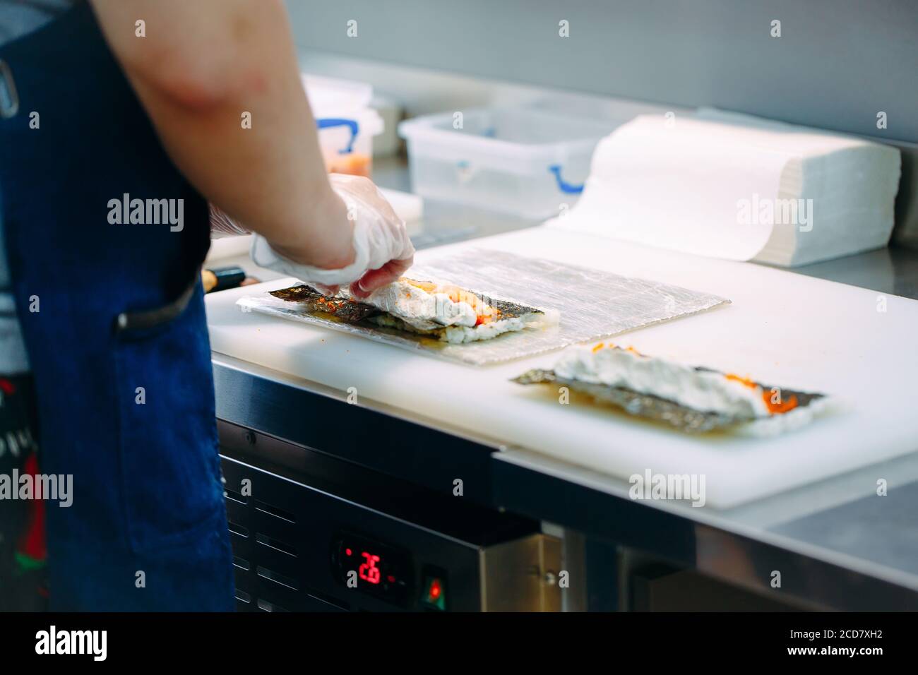 Consegna sushi. Chef mascherati e cuoricissimi preparano il sushi nella cucina del ristorante. Foto Stock