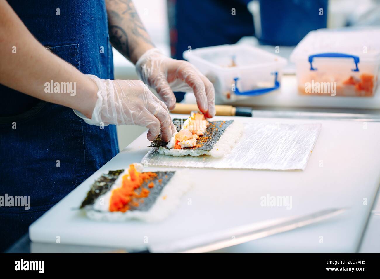 Consegna sushi. Chef mascherati e cuoricissimi preparano il sushi nella cucina del ristorante. Foto Stock