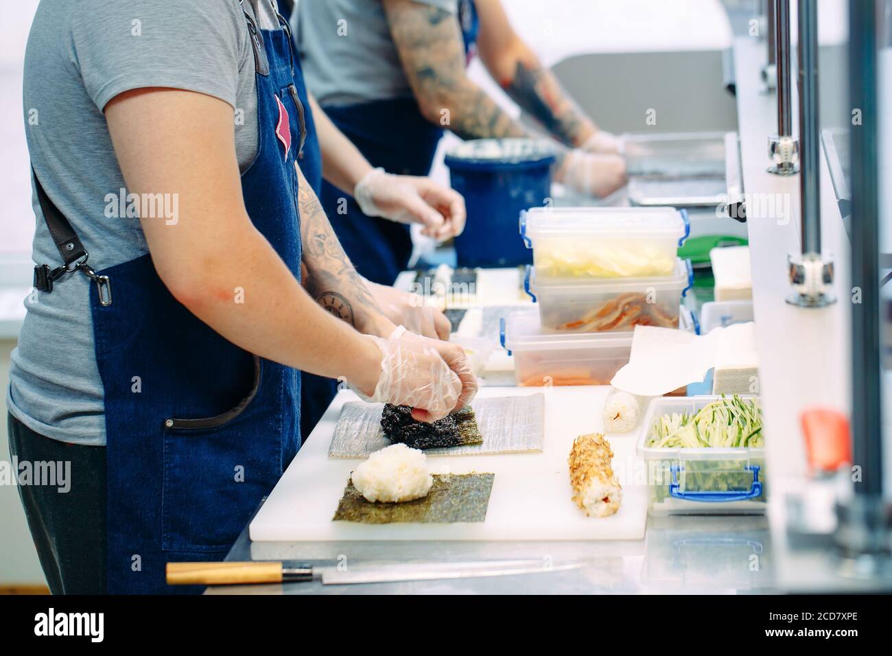 Consegna sushi. Chef mascherati e cuoricissimi preparano il sushi nella cucina del ristorante. Foto Stock