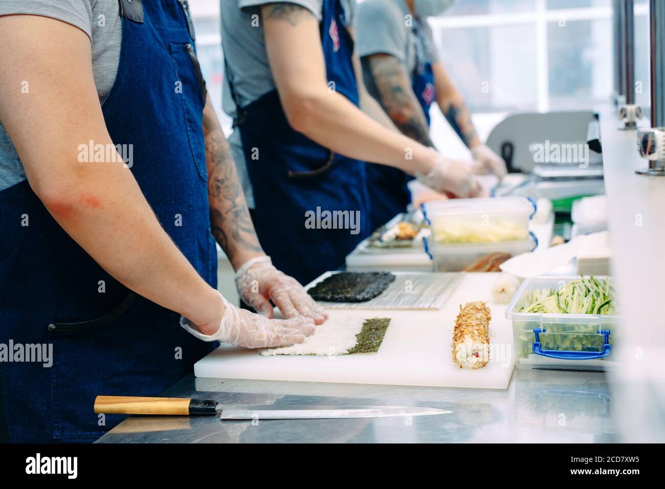 Consegna sushi. Chef mascherati e cuoricissimi preparano il sushi nella cucina del ristorante. Foto Stock