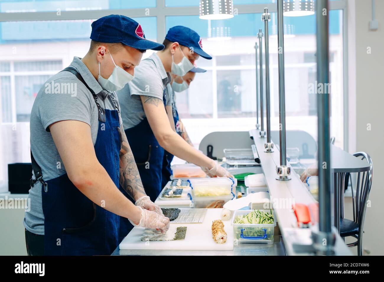 Consegna sushi. Chef mascherati e cuoricissimi preparano il sushi nella cucina del ristorante. Foto Stock