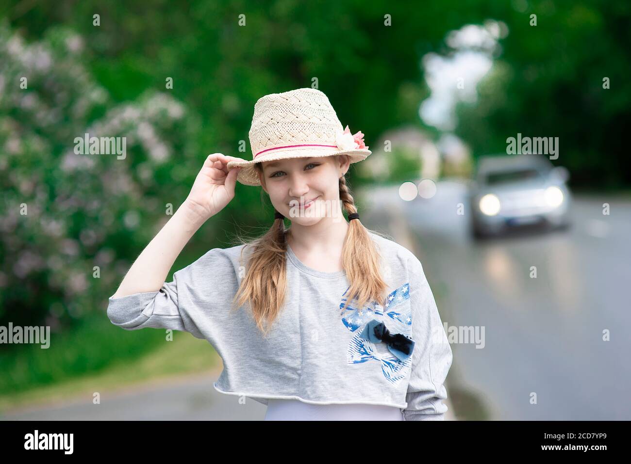 Romantica bella ragazza che indossa un cappello di paglia estivo sorride la strada con un'auto si illumina sullo sfondo Foto Stock