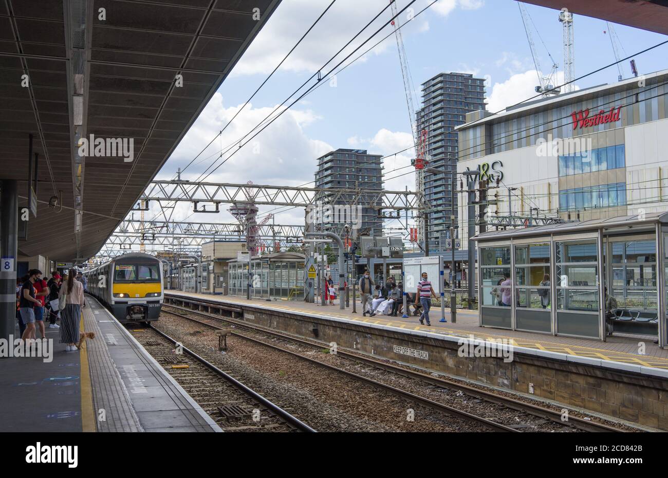 Piattaforme della stazione di Stratford con un treno che entra nella piattaforma. Centro commerciale Westfield sullo sfondo. Londra Foto Stock
