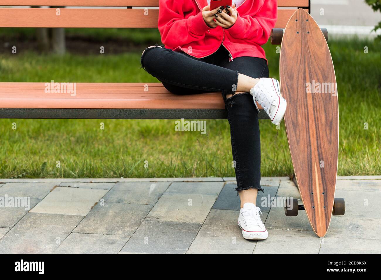 Donna adolescente seduta con skateboard o longboard sulla panchina, utilizzando smartphone e riposo. Foto Stock