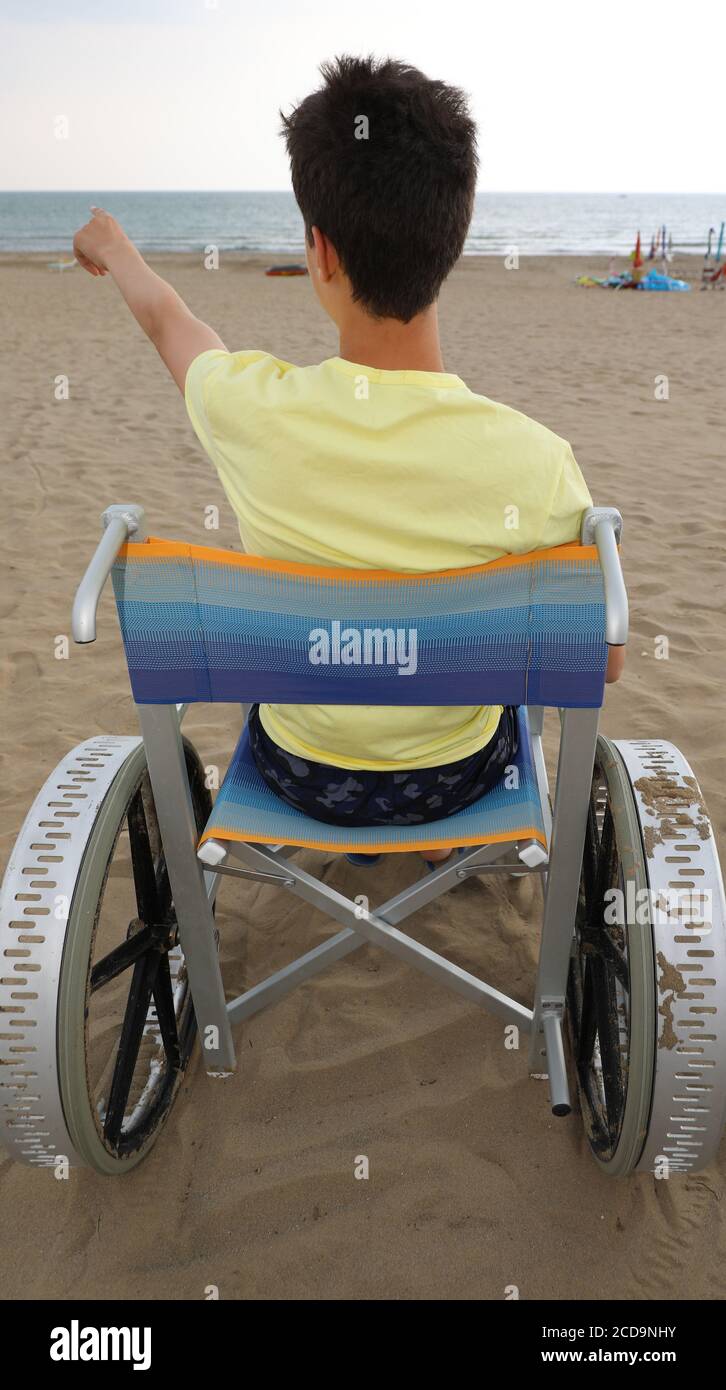 il ragazzo in sedia a rotelle è rivolto verso il mare da la spiaggia Foto Stock