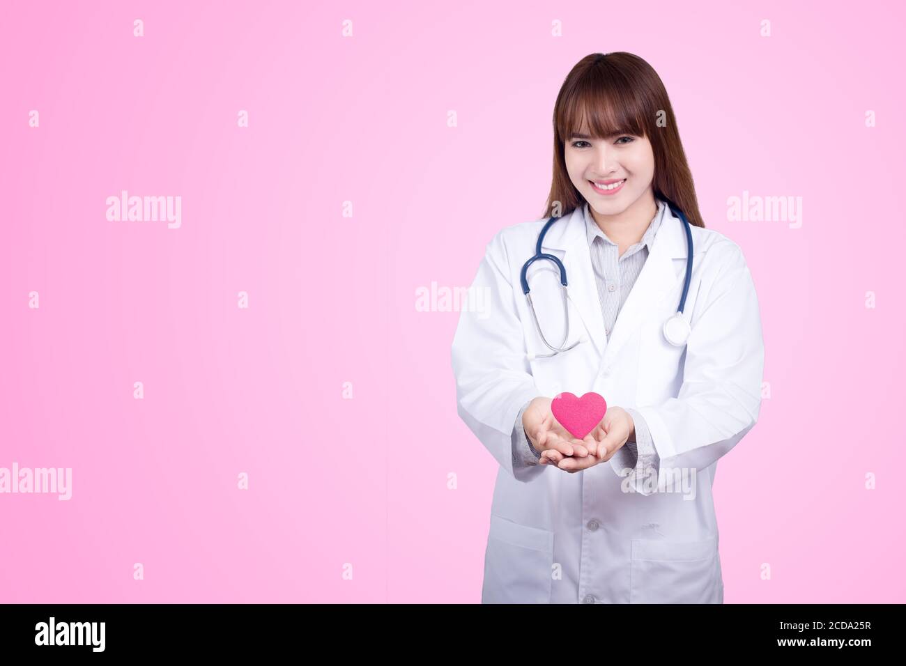 Concetto sano : giovane medico asiatico con cuore rosso in mano. Sfondo rosa Foto Stock