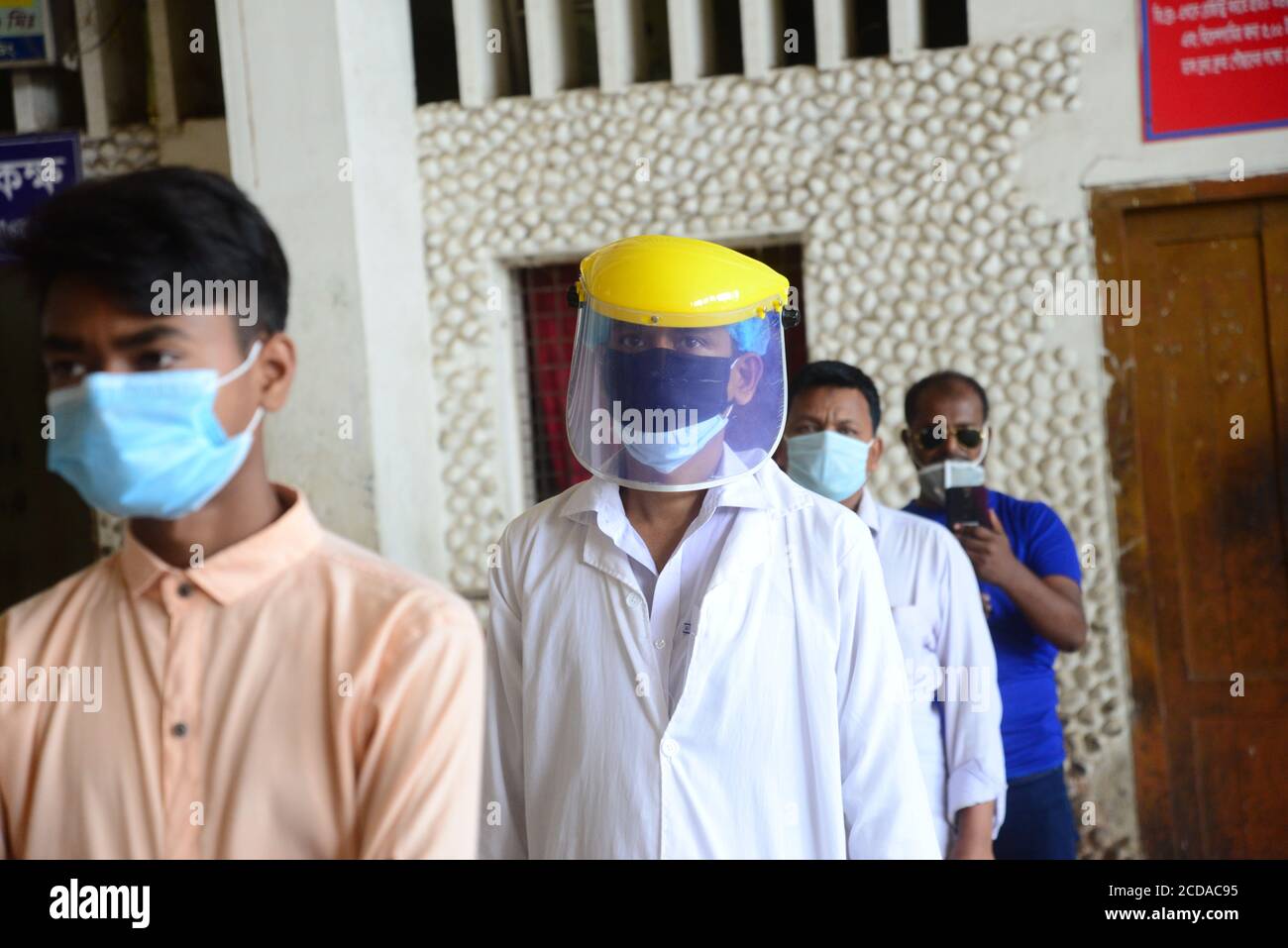 I viaggiatori del Bangladesh che indossano la fila di maschere facciali in su mantengono le attese di distanza sociali per ritirare i biglietti alla stazione ferroviaria di Kamalapur a Dhaka, Banglade Foto Stock