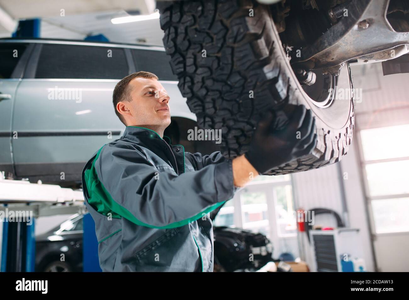 Automobile sollevata nel servizio di automobile per il fissaggio, il lavoratore ripara la ruota, Foto Stock