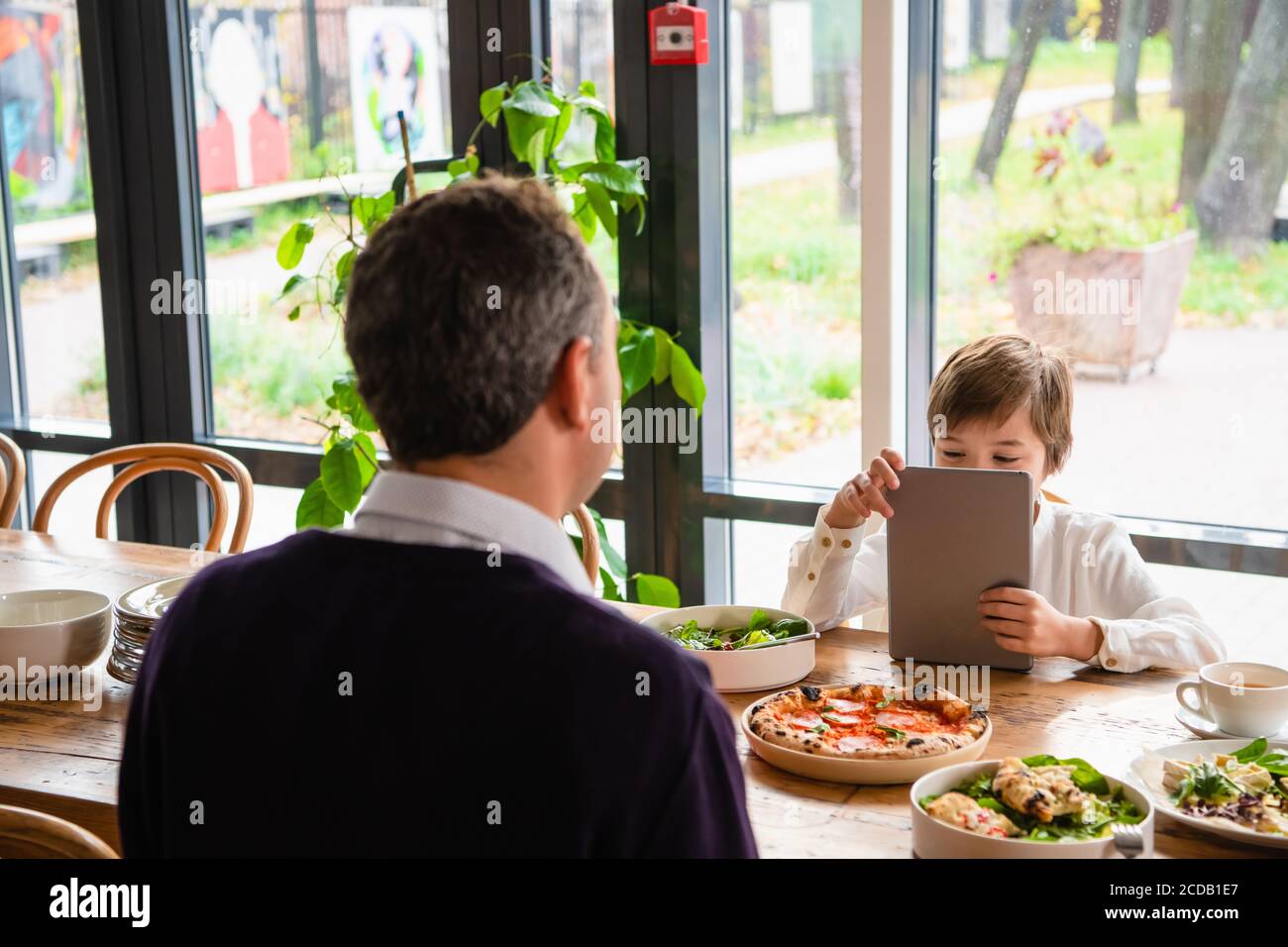 Un ragazzo seduto al tavolo da cucina davanti al padre con un tablet. Foto Stock