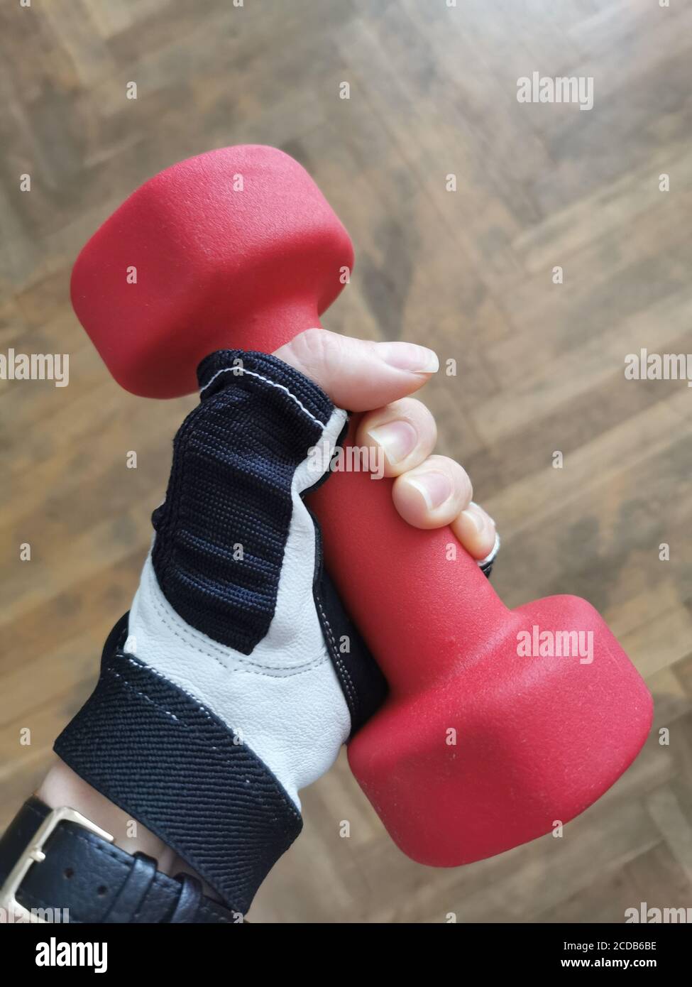 La mano femmina tiene il manubri rosso su fondo di legno. Foto Stock