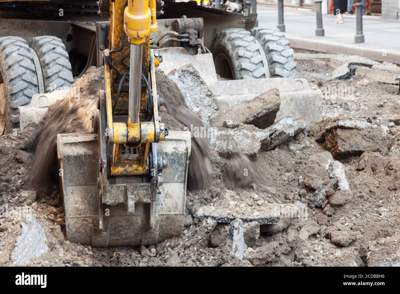 Concentrarsi su ghiaia e sporcizia che escono dalla vetrina di un escavatore meccanico scavatore che lavora in un cantiere di un programma urbano di ristrutturazione stradale. Foto Stock