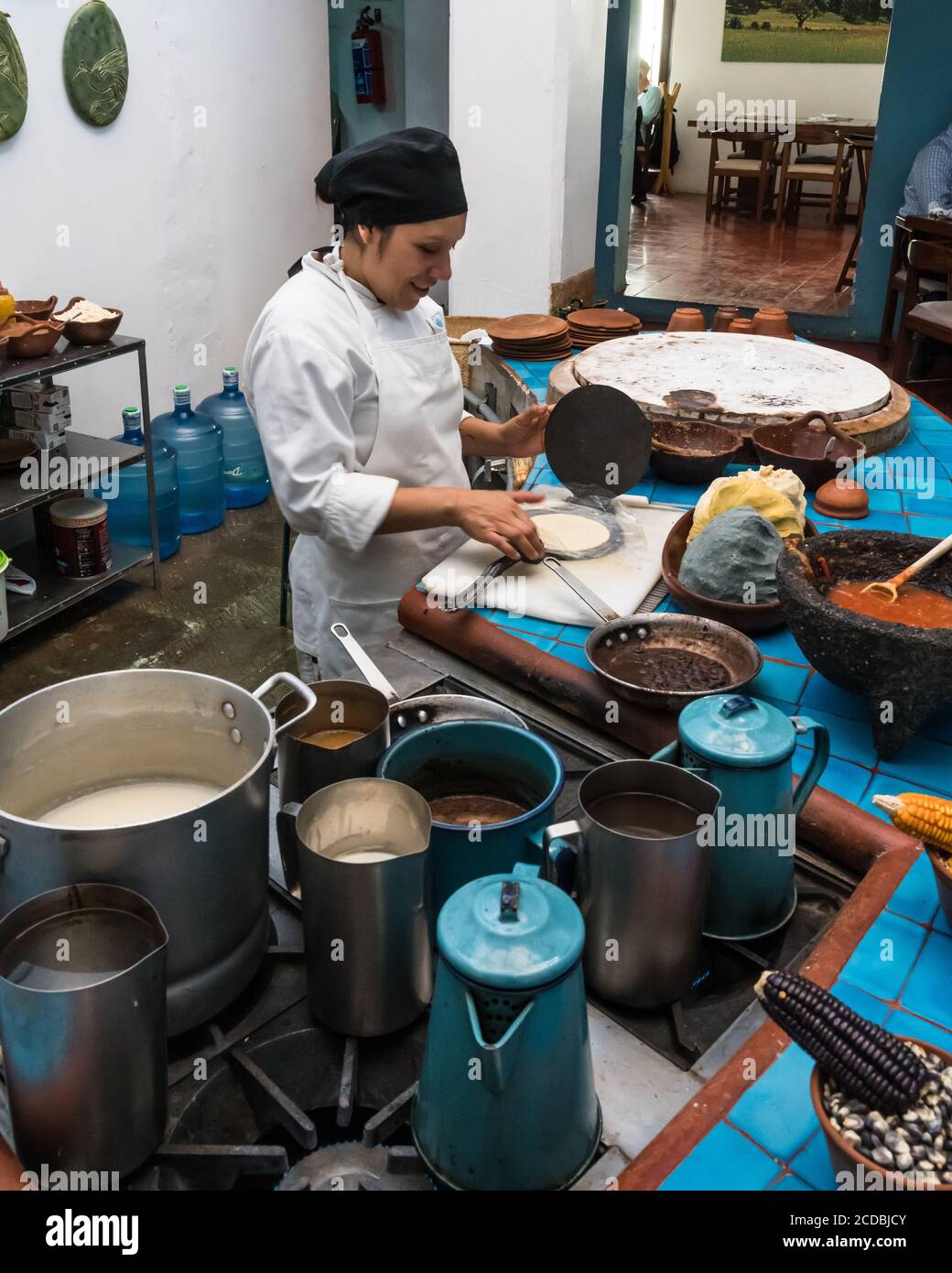 Uno chef crea tortillas in una torciglia metallica in un ristorante a Oaxaca, Messico. Davanti a lei c'è una pasta di mais fatta di blu, giallo e WI Foto Stock