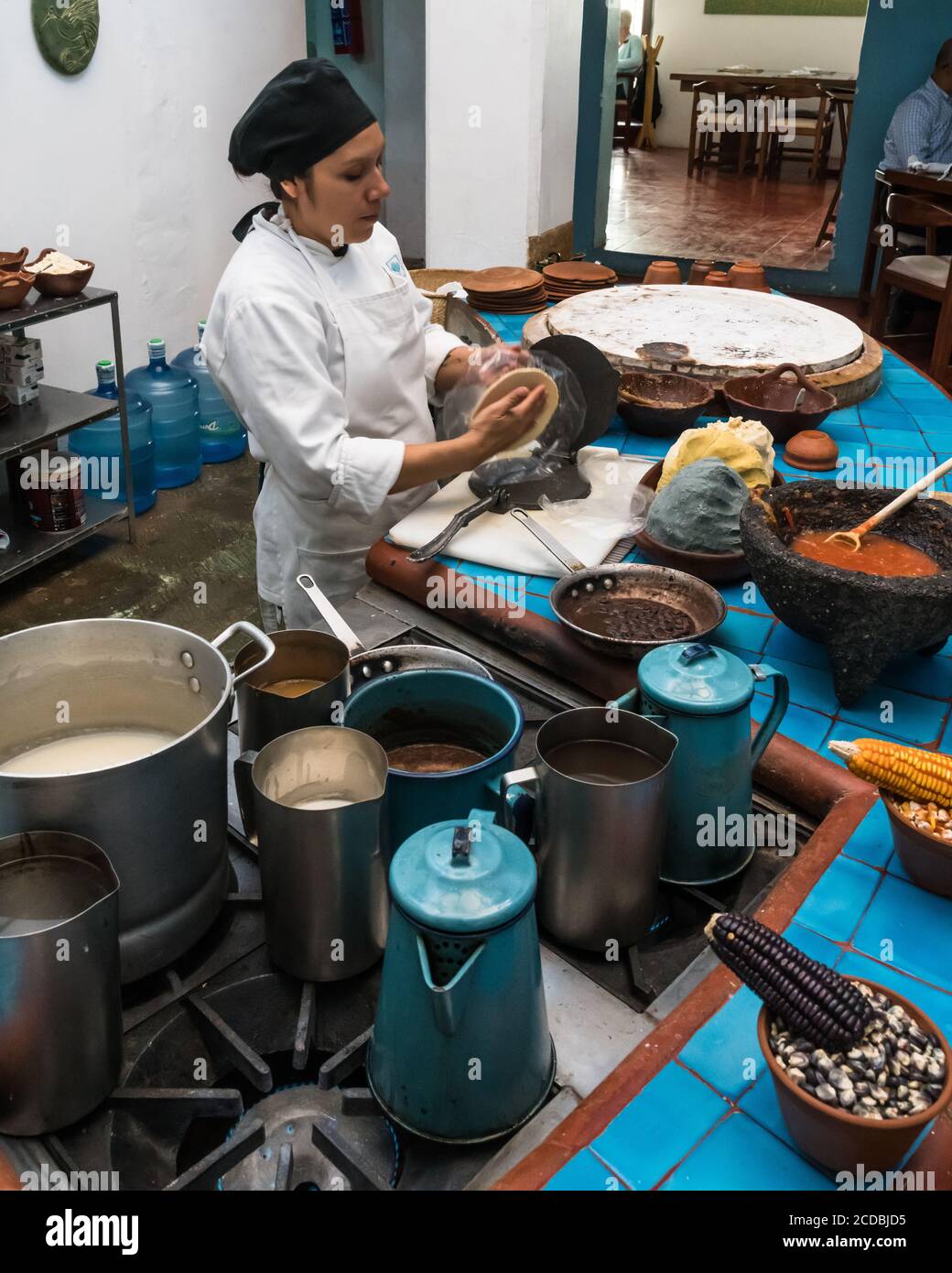 Uno chef crea tortillas in una torciglia metallica in un ristorante a Oaxaca, Messico. Davanti a lei c'è una pasta di mais fatta di blu, giallo e WI Foto Stock