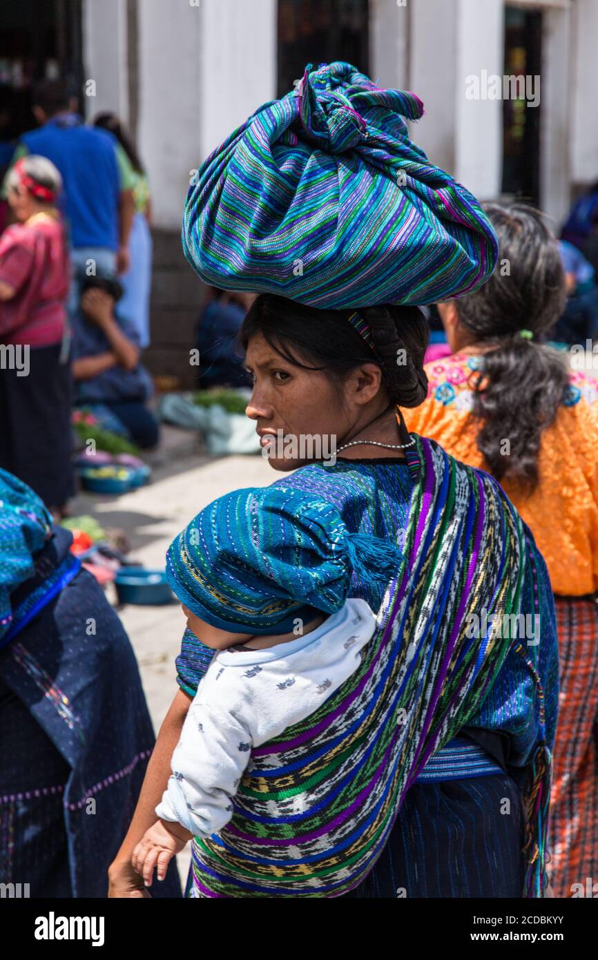 Una giovane donna Maya in abito tradizionale da San Antonio Palopó, Guatemala, porta il suo bambino sulla schiena in una tzute o panno di utilità e porta Foto Stock