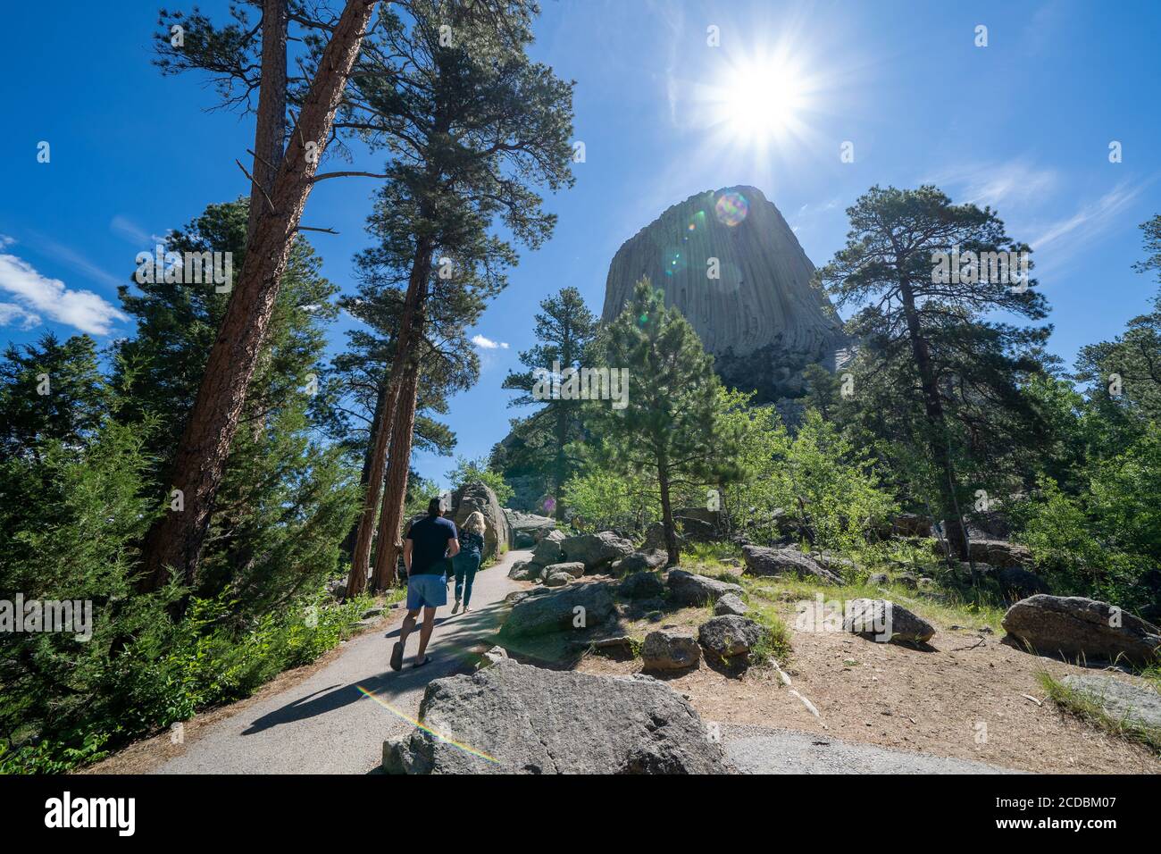 Wyoming, Stati Uniti d'America - 23 giugno 2020: Gli escursionisti turistici camminano verso il Devils Tower National Monument al mattino. SunFlare in foto Foto Stock