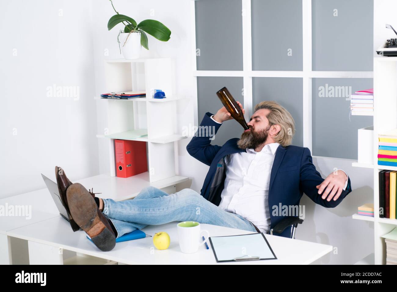Uomo d'affari stanco annoiato che brilica sul posto di lavoro vicino al laptop, lavoro noioso, lavoro di fine lavoro morto, overwork extra dopo l'orario di lavoro, bere alcol. Foto Stock