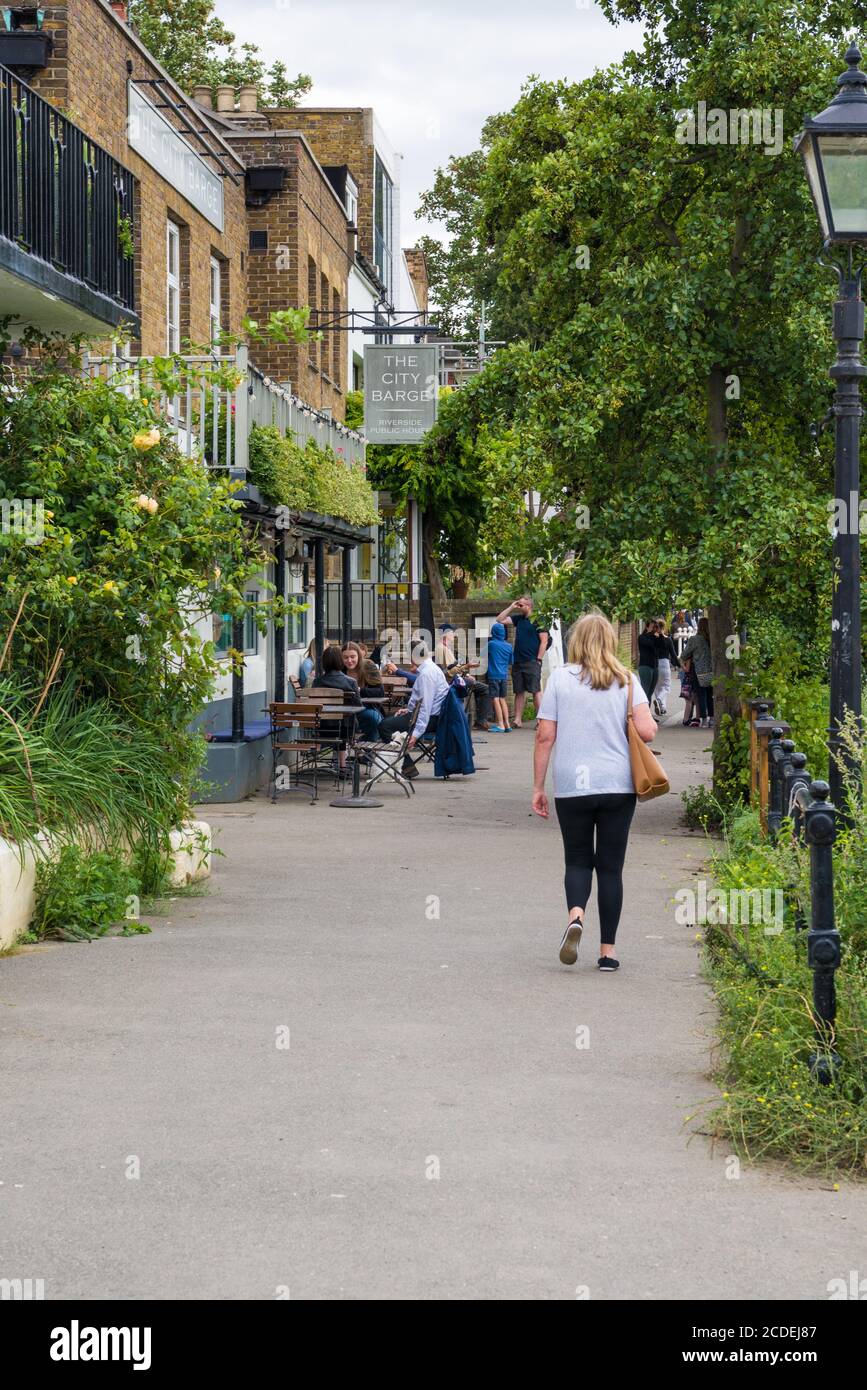 Donna Lone che cammina verso il City Barge, un pub storico del XIV secolo sul lungofiume di Strand-on-the-Green, Chiswick, Londra, Inghilterra, Regno Unito. Foto Stock