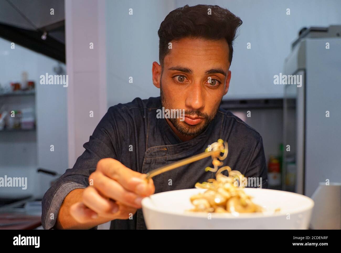 Primo piano di uno chef maschile concentrato che guarnisce il cibo in cucina. Chef caucasico maschile guarnire deliziosi dessert in un piatto presso l'hotel. Faccia di messa a fuoco Foto Stock