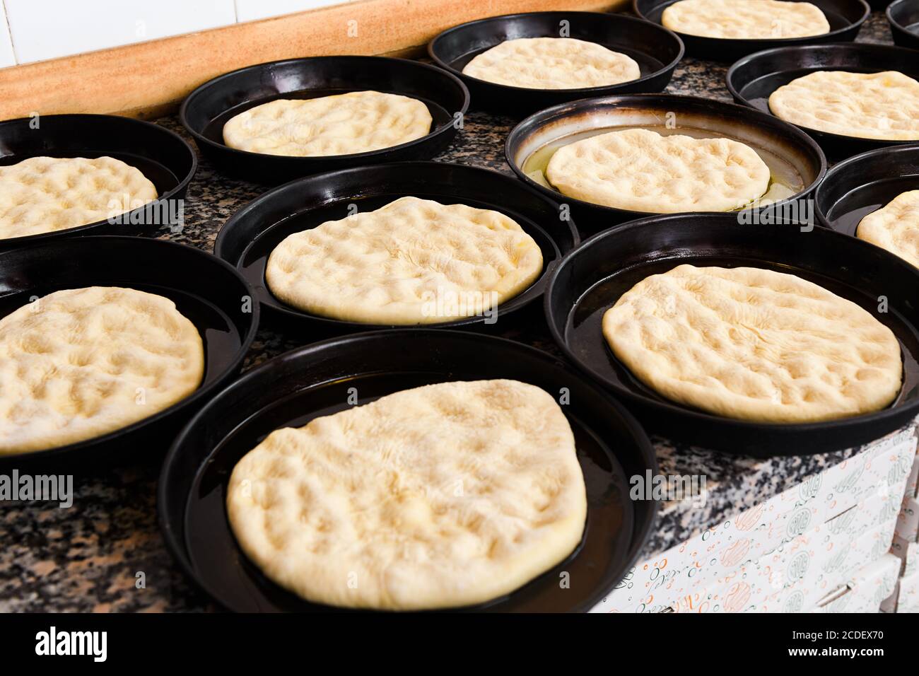 Vaschette per pizza con porzioni di pasta stirata per le basi in piedi pronti su un banco da cucina per l'aggiunta di guarnizioni e guarnizioni assortite Foto Stock
