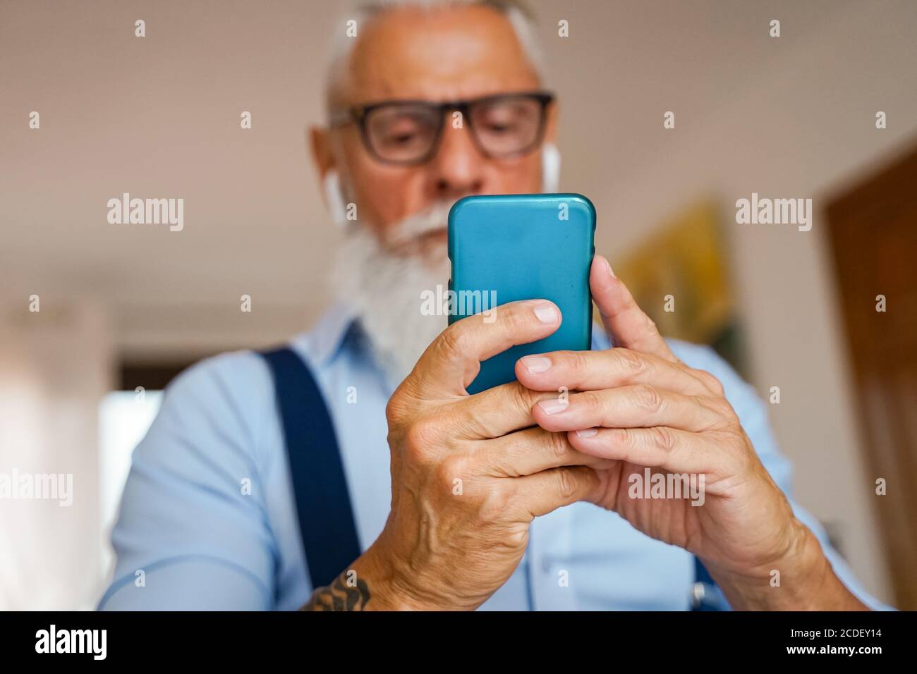 Un uomo attraente in casa, cambia brani e brani sullo smartphone, ascolta la musica con le cuffie wireless. Uomo con barba. Mettere a fuoco le mani - immagine Foto Stock