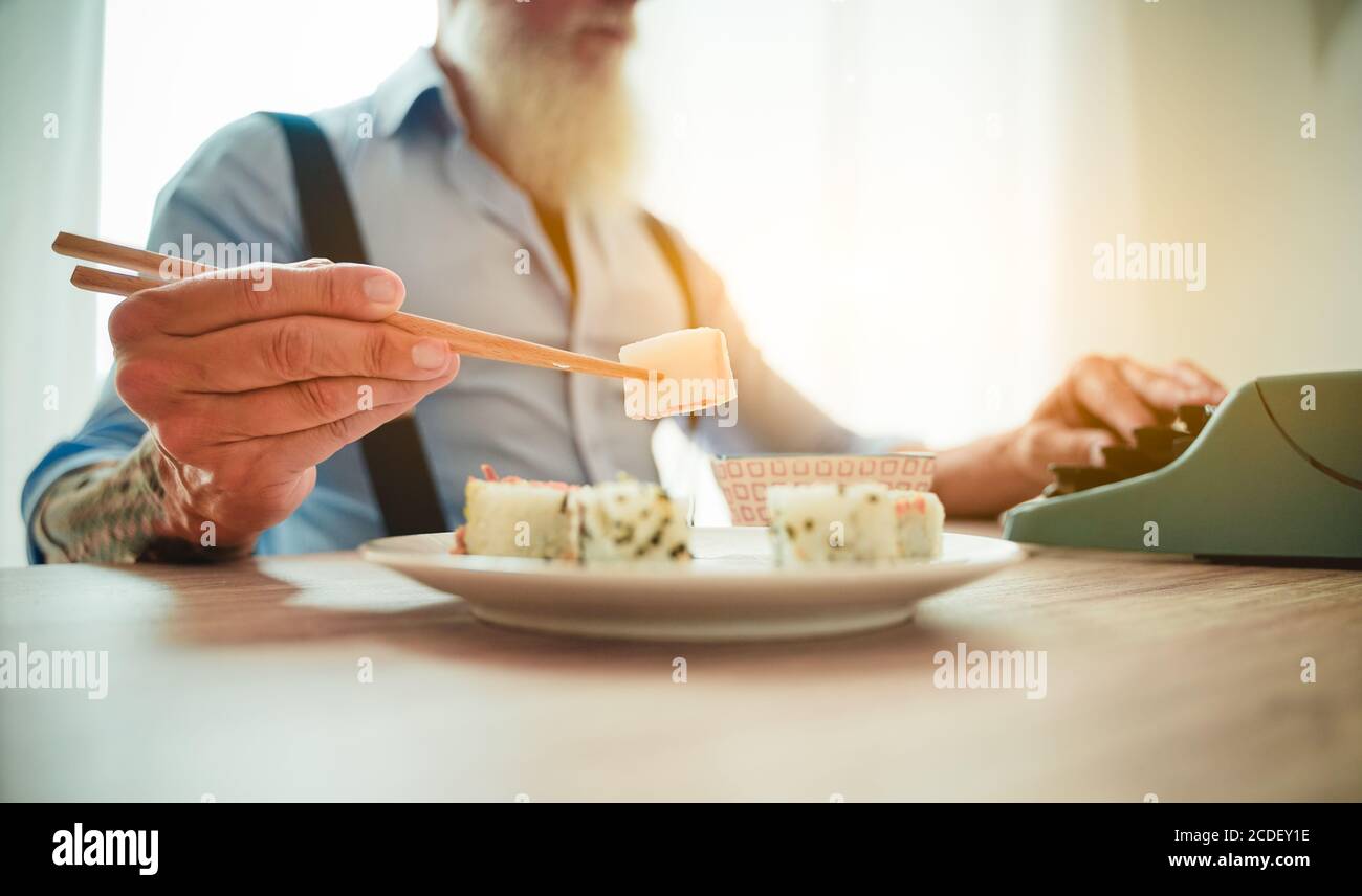 L'uomo si diverte a mangiare sushi asiatico fresco e colorato usando le bacchette. Questo uomo che scrive con la vecchia macchina da scrivere in ufficio. Immagine Foto Stock