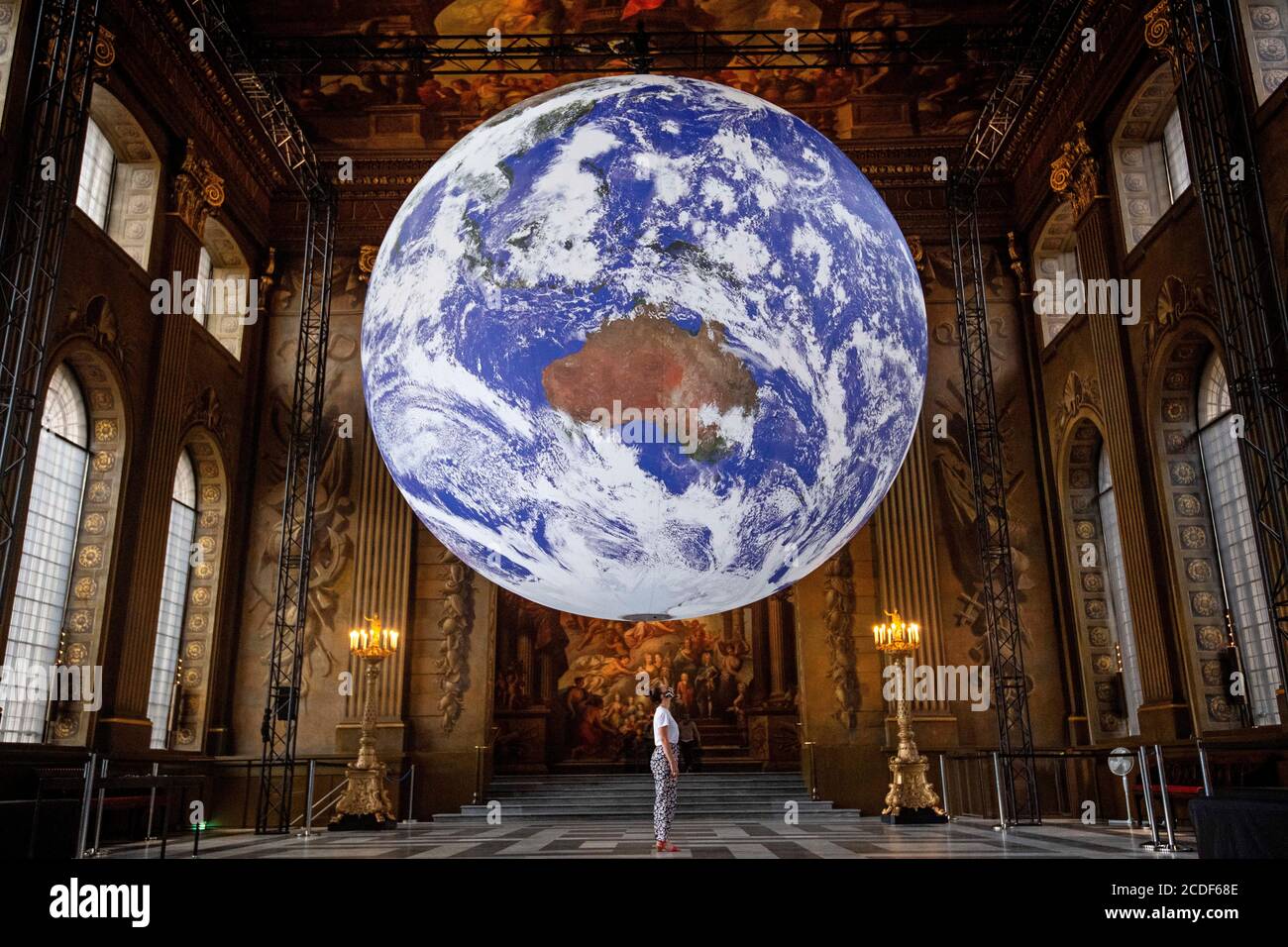 Un membro dello staff guarda le opere d'arte di Luke Jerram Gaia, una replica del pianeta Terra creata utilizzando immagini dettagliate della superficie della Terra della NASA, come viene esposto nella Painted Hall dell'Old Royal Naval College, Greenwich, Londra, come parte del Greenwich+Docklands International Festival del 2020. Foto Stock