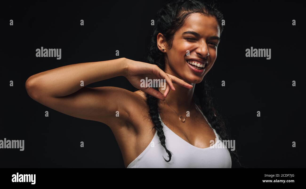 Primo piano di una donna sportiva sorridente in piedi su sfondo nero. Donna allegra in forma nell'occhio winking di umore giocoso. Foto Stock