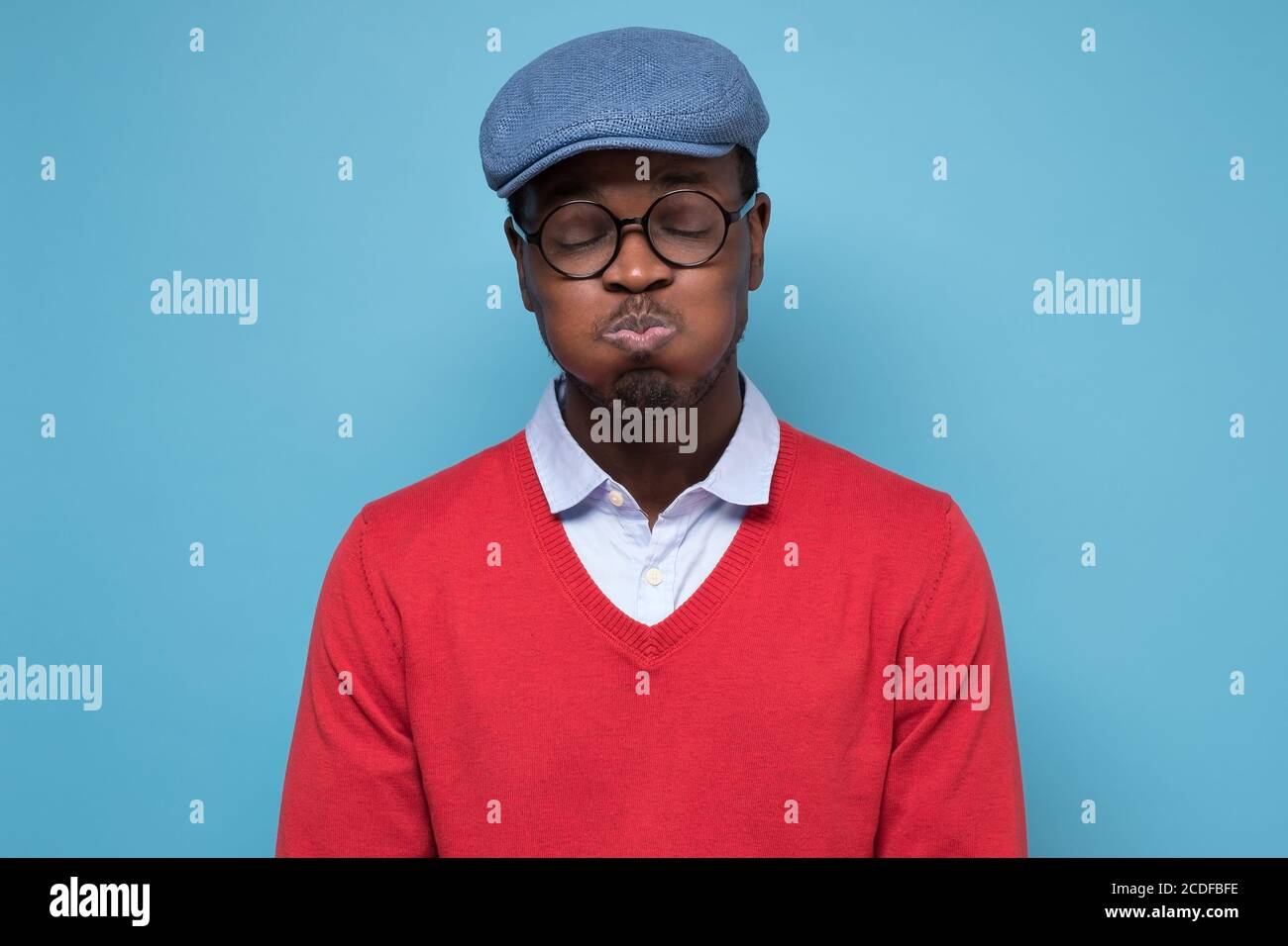 Giovane bell'uomo africano che soffica le guance con il viso divertente che trattiene il respiro. Foto Stock
