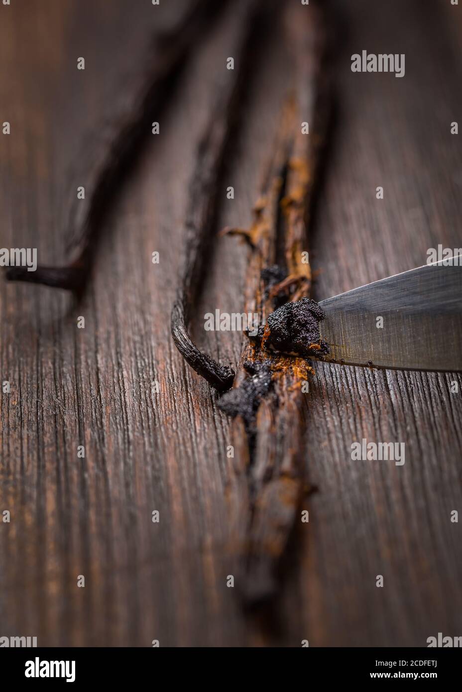 Fagioli alla vaniglia e baccelli di semi con coltello su sfondo di legno. Preparare la vaniglia come ingrediente da forno. Foto Stock