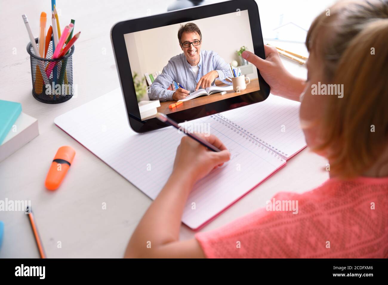 Studente online con insegnante a distanza che prende lezioni attraverso il tablet a casa. Vista posteriore rialzata. Foto Stock