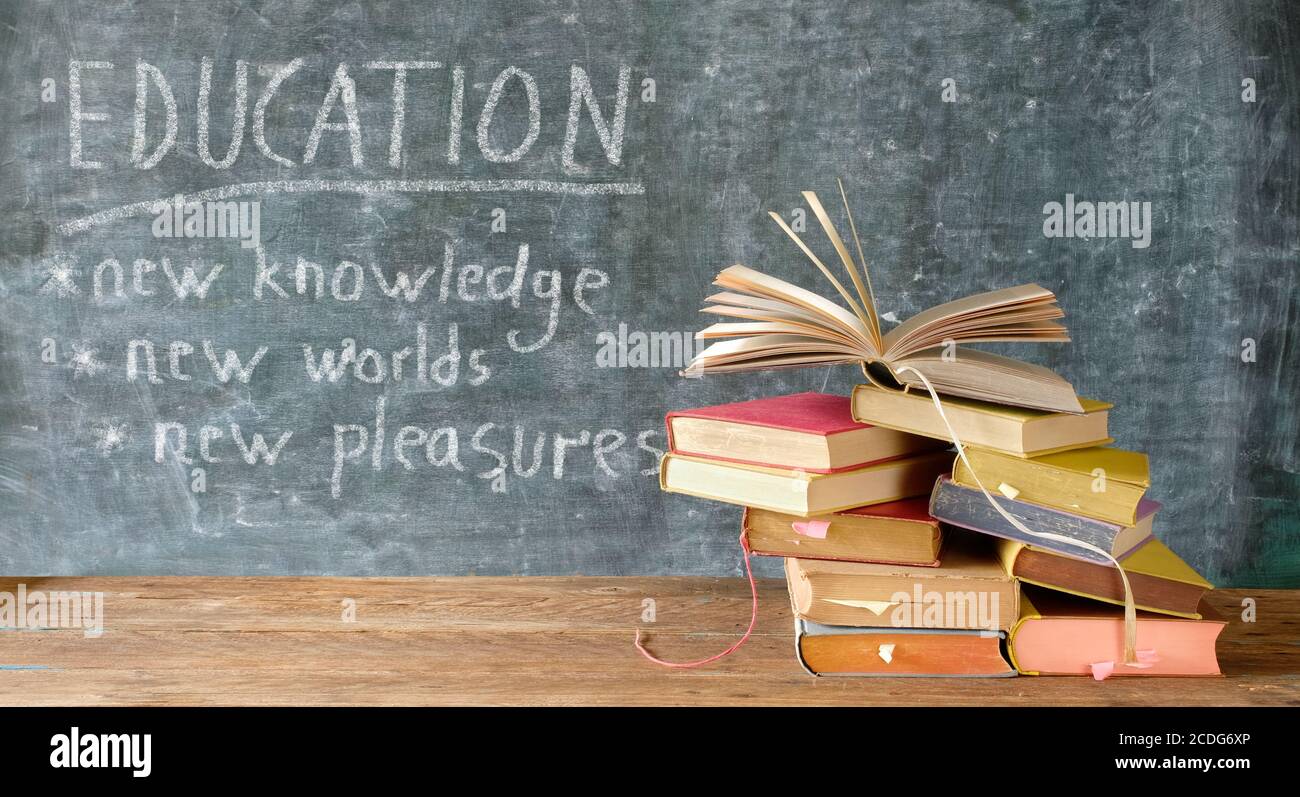 Pila di libri di fronte a una lavagna. Torna a scuola, lettura, educazione, concetto di biblioteca Foto Stock