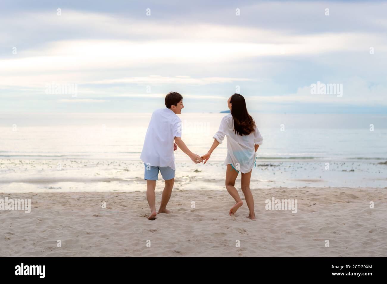 Coppia asiatica innamorata di romantici momenti teneri correre e tenere la mano sulla spiaggia tra il tramonto in Thailandia. Foto Stock