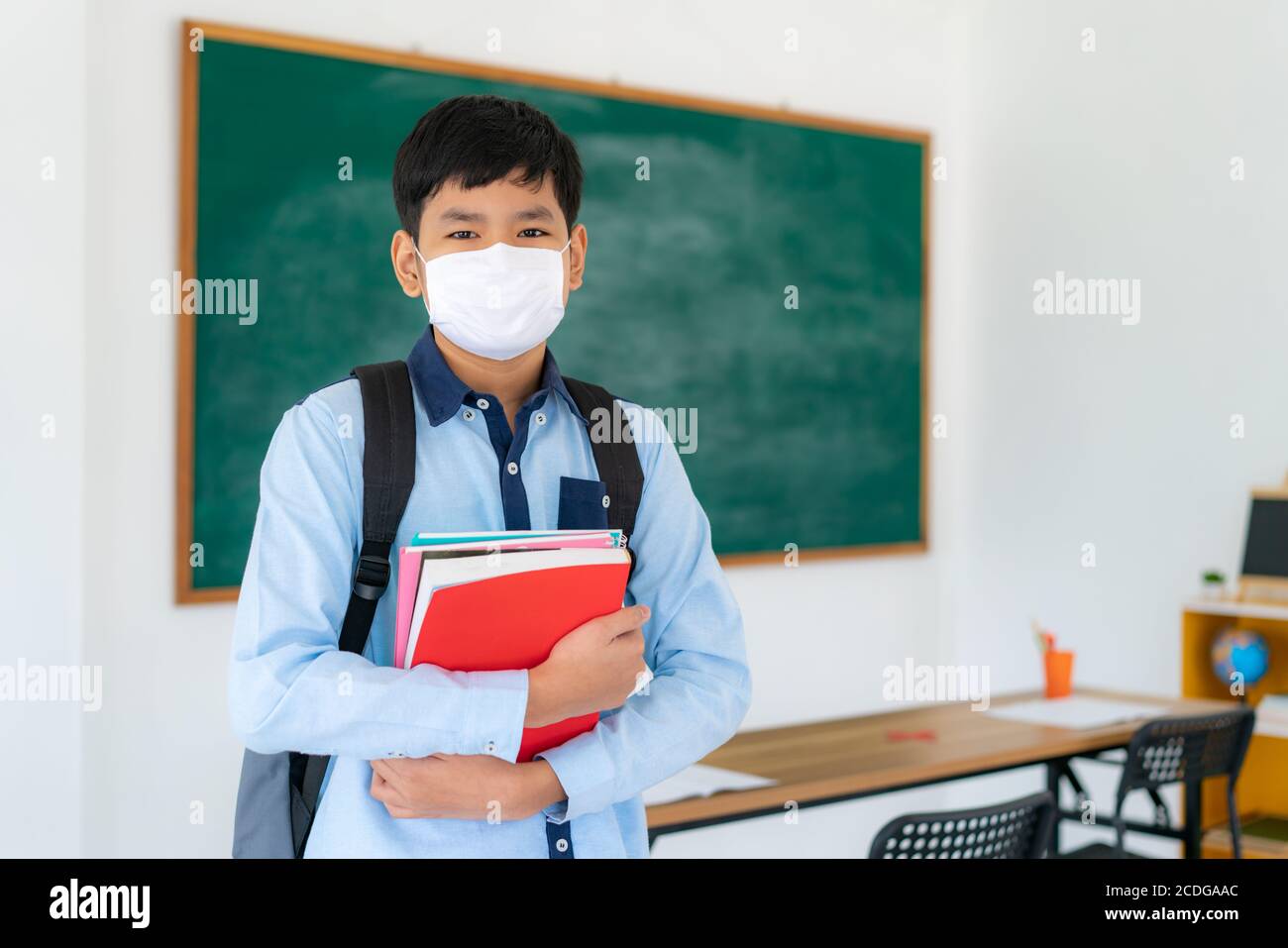 Ragazzi asiatici studenti primari con zaino e libri che indossano maschere per prevenire lo scoppio di Covid 19 in classe mentre torna a scuola riaprire il loro sc Foto Stock