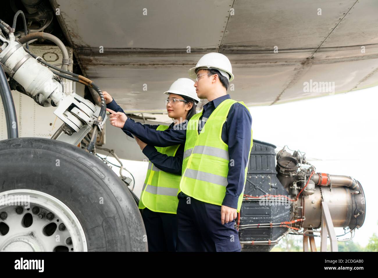 Uomo e donna asiatici ingegnere manutenzione aerei team riparazioni, correzioni, modernizzazione e ristrutturazione in aereo di fronte da in aeroporto. Foto Stock