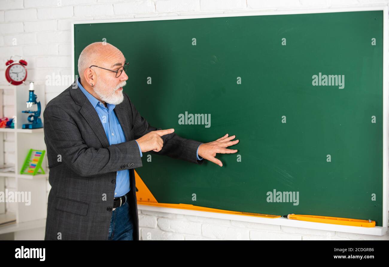 guarda e impara. l'istruzione nella scuola moderna. l'uomo con il bearded mostra qualcosa. copia spce. l'insegnante senior spiega il soggetto alla lavagna. l'insegnante di geografia. l'aula con la mappa. torna a scuola. Foto Stock