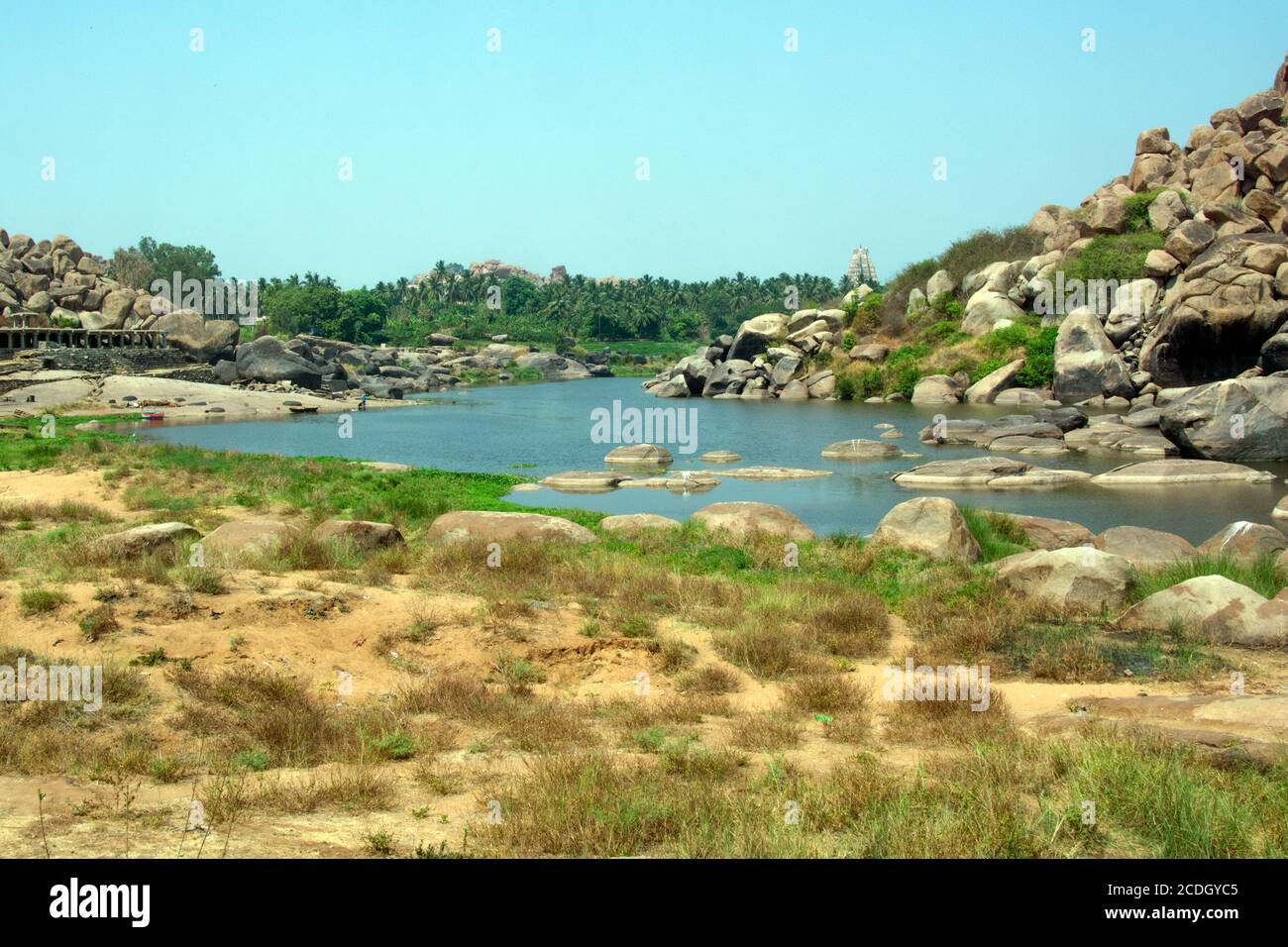 Nella distanza tra l'ambiente arido e il paesaggio roccioso del fiume Tungabhadra, si può vedere il famoso Tempio Birupaksha di Hampi. Foto Stock