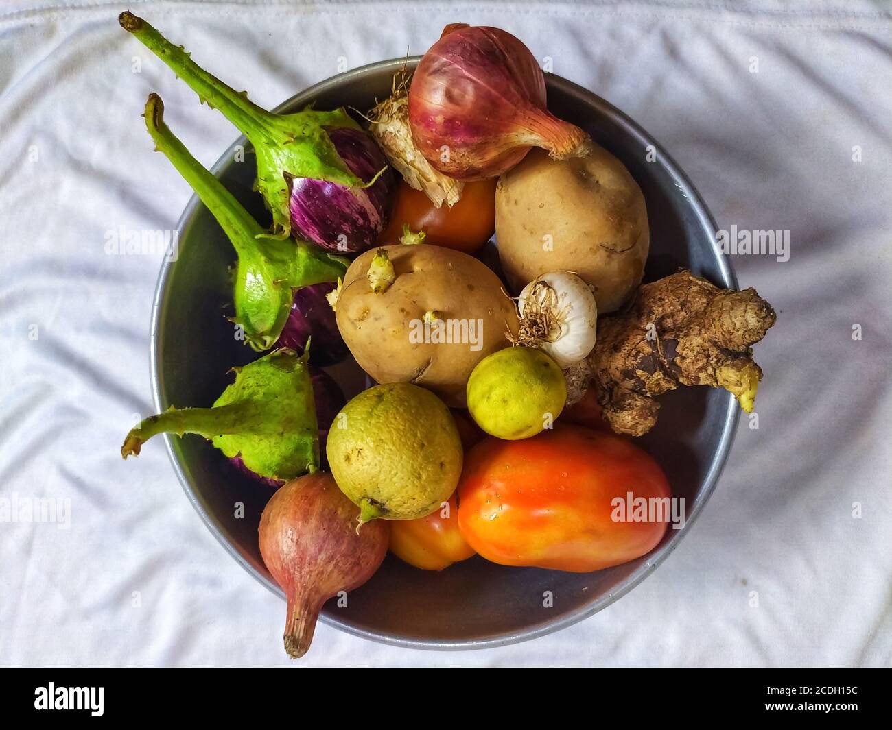 Un delizioso mucchio di verdure include pomodoro, brinjal, patate, cipolla, aglio. Limone e zenzero sono isolati su tessuto piegato di colore bianco Foto Stock