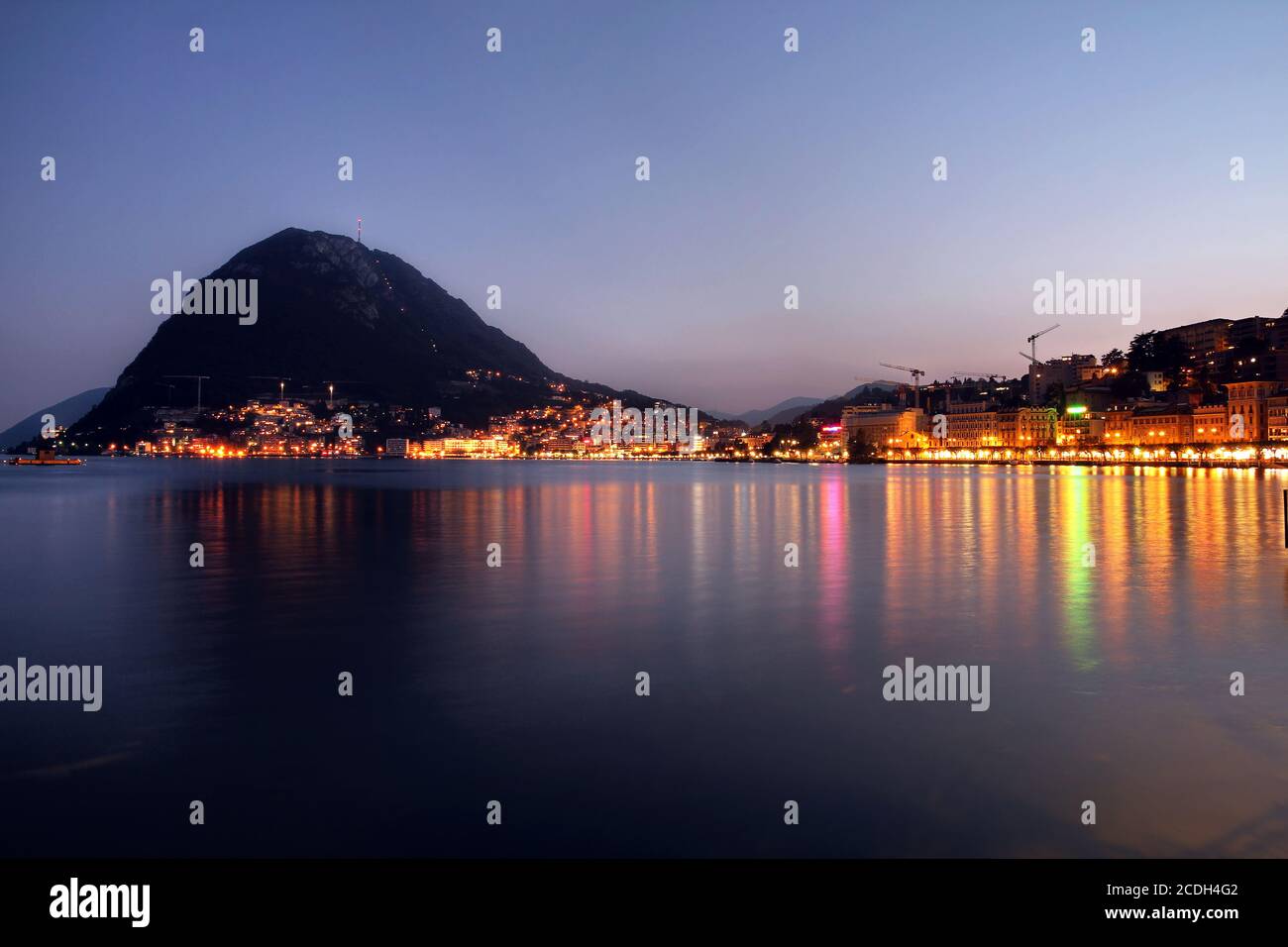 Tramonto sulla città di Lugano nella Svizzera meridionale (Cantone Ticino), con Monte San Salvatore dalla riva del lago. Foto Stock