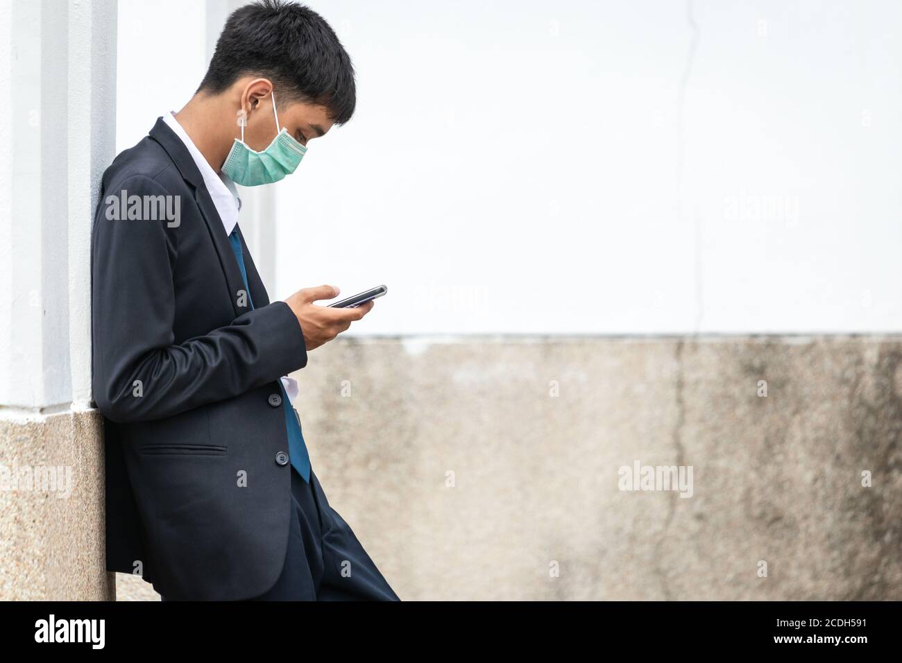 Un bel giovane uomo d'affari asiatico che usa lo smartphone. Giovane e attraente uomo d'affari asiatico che indossa una maschera che pende contro il muro. Foto Stock