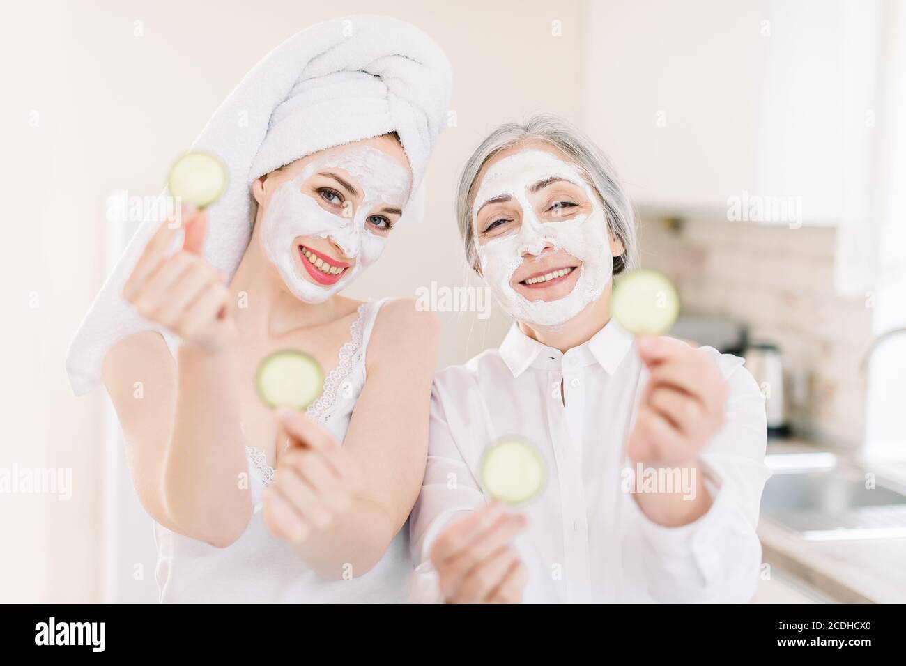 Routine di cura della pelle di mattina, giornata di cure termali di famiglia. Bella donna grigio capelli anziani e la sua giovane nipote attraente che fa maschere facciali in argilla e posa Foto Stock